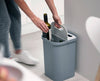 A woman throwing wine bottles into the trash bin situated in the kitchen