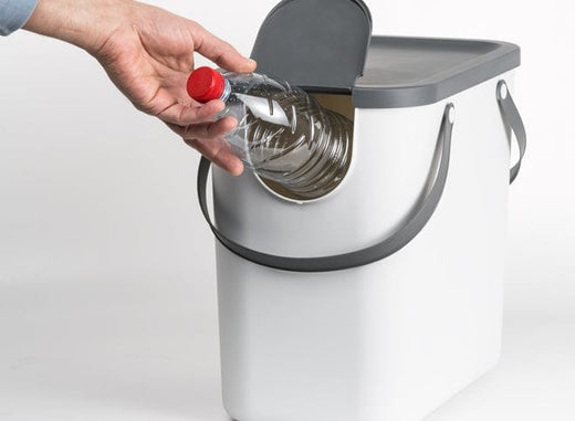 White recycling bin with lid flap in the open position with a bottle being placed through it