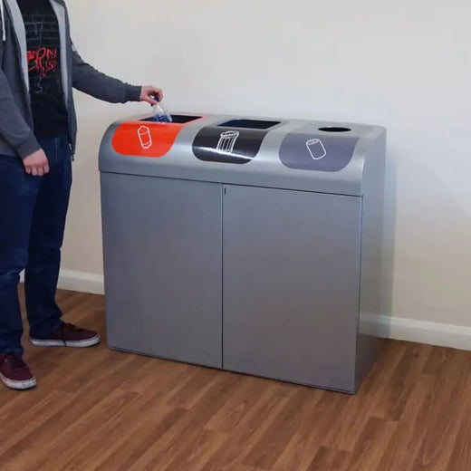 Triple stream recycling bin placed on the hallway. A man throwing a plastic bottle into the orange waste stream.