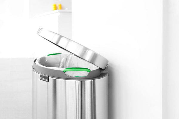 Brabantia flat back waste bin with the lid open, sitting against a wall