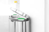 Brabantia flat back waste bin with the lid open, sitting against a wall