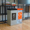 Dual compartment recycling station.  General waste with silver body and black lift up lid, mixed recycling with transparent body and orange propeller lid