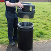 A man removing the top lid from the plastic covered recycling bin in an outdoor setting.