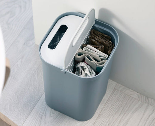 a grey bodied recycling caddy with the left side lid closed, and the right side unlidded, unveiling the plastic bottles within.