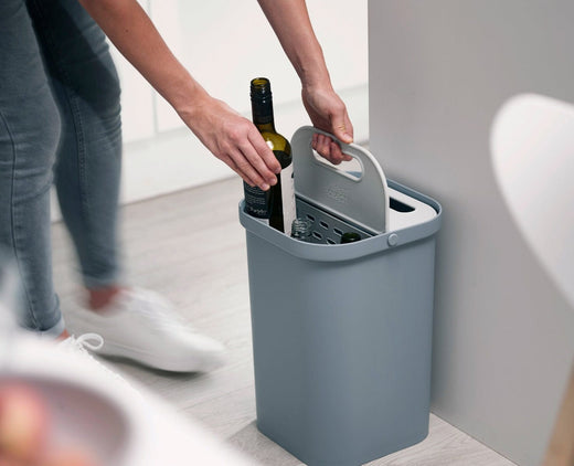 a woman discarding wine bottles into a recycling caddy located in the kitchen.