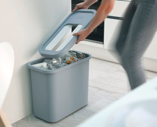 A lady removing the lid of the recycling bin in grey color.