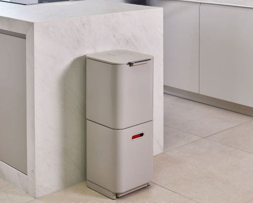 stone colored waste bin is placed beside the kitchen counter. 2 compartments are stacked.