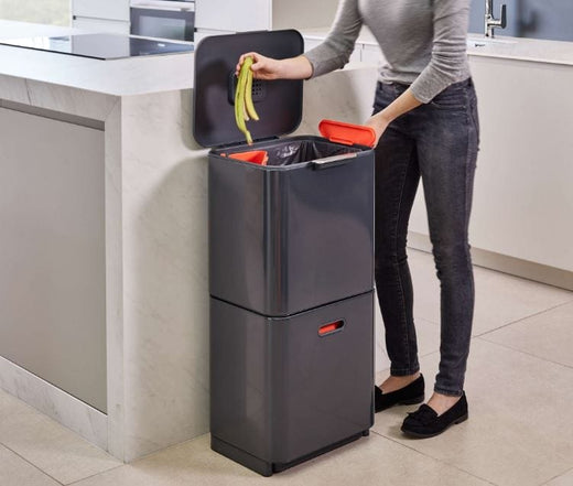 A woman throwing a banana peel into the upper trash bin located in the kitchen.