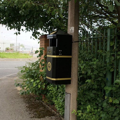Side angle of closed top litterbin mounted to a lampost.  Black body with apex lid and decorative gold banding