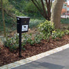 Dog post mountable litter bin in location with black body, and black lift up lid with white dog waste iconography to the body