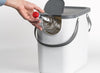 White recycling bin with lid flap in the open position with a bottle being placed through it